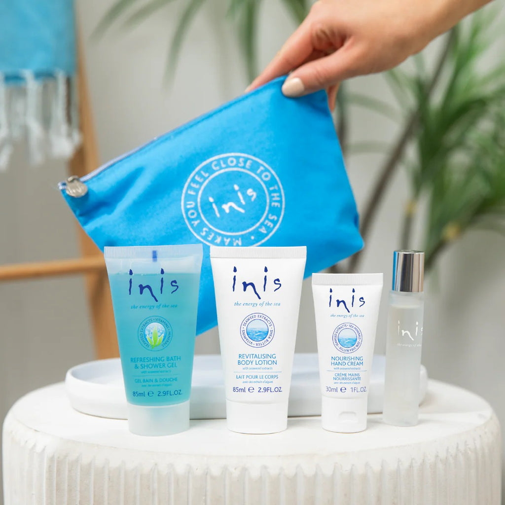 Inis Voyager Set four travel-size products on white pedestal with Inis blue zip bag held behind in home setting